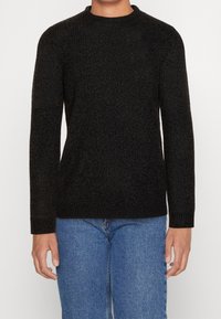 Schwarzer gestrickter Pullover mit Rundhalsausschnitt und langen Ärmeln, strukturierter Stoff, kombiniert mit blauen Jeans.