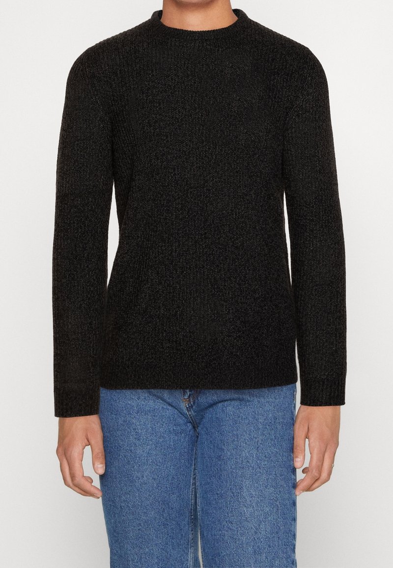 Schwarzer gestrickter Pullover mit Rundhalsausschnitt und langen Ärmeln, strukturierter Stoff, kombiniert mit blauen Jeans.