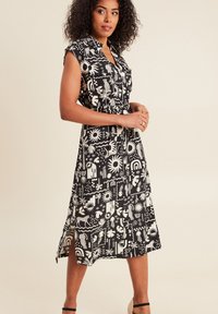 Schwarzes und weißes gemustertes Kleid mit kurzen Ärmeln, kragenförmigem Ausschnitt, tailliertem Bund und plissiertem Rock mit Sonnen- und Tiermotiven.