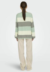 Pull en tricot rayé de couleur vert menthe, blanc et gris, avec une coupe décontractée, des manches longues et une texture côtelée ; associé à un pantalon beige clair.