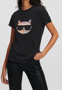 T-shirt nera con una grafica colorata di un volto di gatto con occhiali da sole. Maniche corte e tessuto morbido con una vestibilità rilassata.