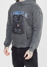 Felpa grigia con un grande grafico di una pantera nera, tasca a marsupio frontale e polsini a coste. Il materiale sembra morbido con una texture consumata.