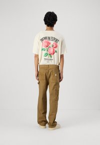 T-shirt graphique beige avec des roses roses et du texte dans le dos, associé à un pantalon cargo beige avec poches latérales et une coupe décontractée.