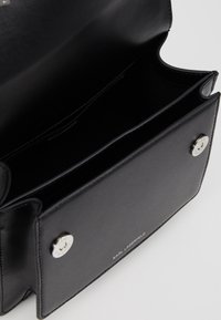 Borsa in pelle nera Karl Lagerfeld aperta per mostrare due scomparti principali con chiusure a scatto argentate su uno sfondo bianco.