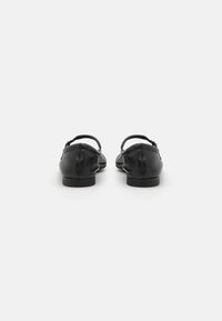 Black leather flats with a rounded toe, thin straps, low heel, and smooth texture. Features a small buckle detail on the strap.