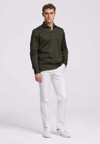 Donkergroene polo met lange mouwen en een drieknoopsluiting, gecombineerd met witte slim-fit pantalon en witte sneakers. Soepele katoenen textuur.