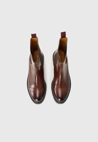 Bottines en cuir marron avec des panneaux élastiques sur les côtés, bout rond et design texturé à l'avant. Présente une languette à l'arrière.