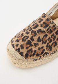 Cipele sa leopard uzorkom, bez kopčanja, sa gornjim dijelom od mekanog antilopa, okruglim vrhom i dekorativnim jute rubom. Imaju teksturiranu površinu i vidljive šavove.