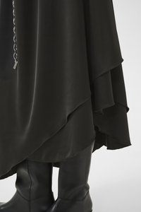 Jupe noire à plusieurs couches avec un design fluide, dotée d'une texture lisse et d'un ourlet asymétrique. Associée à des bottes en cuir noires hauteur genou.