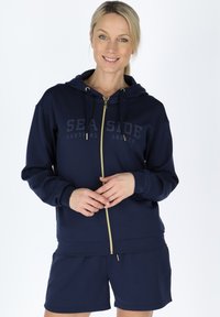 Navy zip-up hoodie with gold hardware, featuring a front logo print and ribbed cuffs, paired with matching shorts in a soft material.