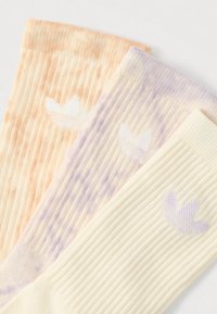 Three pairs of socks in pastel colors: orange, beige, and light yellow. Ribbed texture with a small logo on each sock in white or purple.