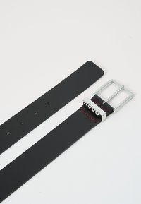 Ceinture en cuir noir avec boucle en métal argenté. Présente des coutures rouges et plusieurs trous de réglage. Design minimaliste avec texture lisse.