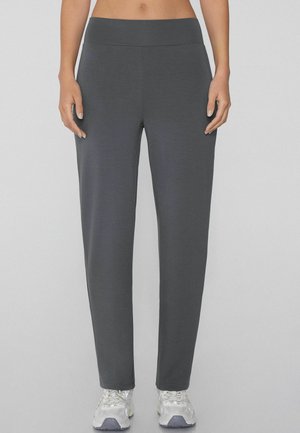 Pantalones deportivos grises hechos de una tela suave, con una cintura elástica ancha y un diseño de pierna recta, combinados con zapatillas blancas.