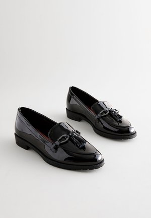 Fekete lakkozott bőr mokaszinok lapos talppal, díszes masnival és bojttal az elején, sima, fényes felülettel.