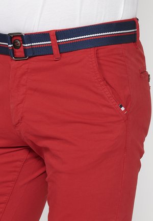 Pantalones de algodón rojos con un cinturón azul marino que tiene acentos de rayas blancas y rojas, bolsillos laterales y una pequeña etiqueta de marca en el bolsillo.