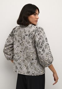 Blusa grigia con fantasia floreale e maniche a sbuffo, caratterizzata da una superficie liscia e motivi a contrasto in nero e crema.