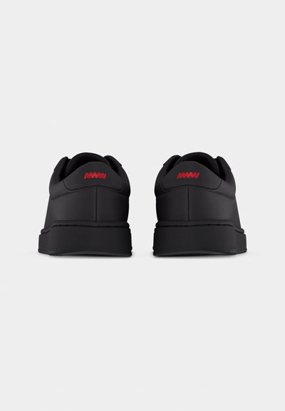 Paire de baskets noires vues de dos, avec un logo rouge en zigzag sur la languette du talon et des semelles épaisses noires.