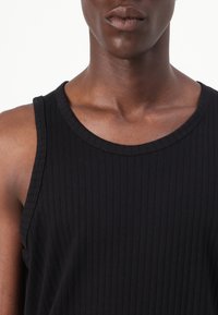 Musta ribbed ilmanhiha-toppi, jossa on pyöreä pääntie, valmistettu pehmeästä puuvillakankaasta, jolla on sileä rakenne ja istuva siluetti.