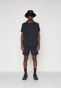 Black athletic outfit featuring a sleeveless zip vest, t-shirt, shorts, and bucket hat. Material is lightweight, with sunglasses as notable detail.