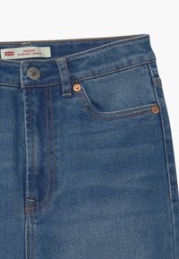 Jeans de mezclilla azul con un corte recto en los tobillos. Cuenta con un bolsillo frontal, remaches de cobre y una etiqueta de marca en la cintura.
