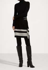 Svart stickad polotröja, kjol ovanför knäet med svarta och grå ränder, sidspännen och fransdetaljer, i kombination med knähöga svarta stövlar.