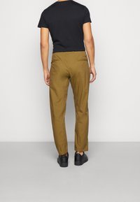 Hnědé kalhoty s přímým střihem, vybavené zadní kapsou a hladkou texturou, doplněné černou krátkou košilí a černými teniskami.