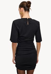 Robe noire ajustée en tissu doux, avec manches courtes, dos avec ouverture en goutte d'eau, et détails froncés sur les côtés.