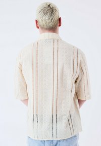 Beige shirt met korte mouwen en opengewerkt patroon, met circulaire en driehoekige ontwerpen, textiele stof en eenRelaxte pasvorm.