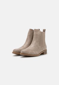 Bottines en daim beige clair avec des panneaux élastiques sur les côtés et un petit talon empilé. Texture lisse avec des détails de couture minimaux.