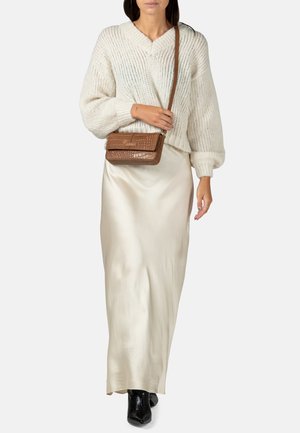 Romige chunky-gebreide trui, satijnen beige maxi rok en zwarte enkellaarsjes. Kleine bruine tas met krokodillenprint als crossbody met een lange schouderband.