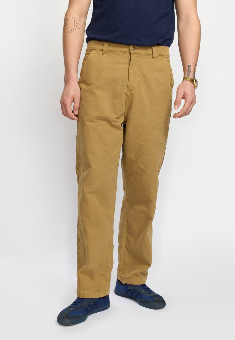 Pantaloni khaki in cotone con design a gamba dritta, dotati di zip e chiusura a bottone. Indossati con una t-shirt blu navy e scarpe da ginnastica blu.