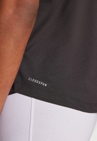 Svart sporttshirt med slät textur, skuren nära midjan, med "CLOUDSPUN"-logotyp i vitt vid fållen. Inga markanta mönster.