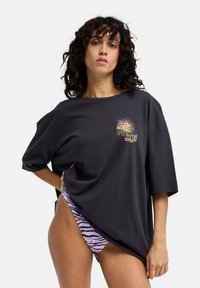 Μαύρο υπερμεγέθες βαμβακερό T-shirt με γραφικό σχέδιο μπροστά. Συνδυάζεται με ροζ και μαύρο μαγιό σλιπ με ρίγες ζέβρας. Καθημερινό, άνετη γραμμή.