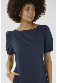 Navy modrá šaty so štvorcovým výstrihom a vypuklými krátkymi rukávmi. Hladká látka s bočnými vreckami a sánkovými detailmi na rukávoch.