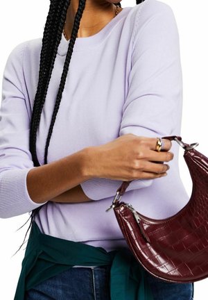 Hellvioletter Pullover mit gerippten Bündchen, kombiniert mit dunklen Jeans und einer grün gebundenen Jacke. Burgunderfarbene Handtasche mit Krokoprägung in der Hand gehalten.