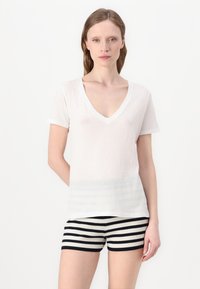 Hvid V-hals t-shirt med korte ærmer og en tekstureret, let gennemsigtig finish, parret med sort-hvide stribede ribbede shorts.