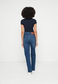 Sinised teksapüksid sirge säärega, millel on nahast plaastriga detail tagumisel vöökohal ja kaks tagataskut. Sobitatud keha järgiva meresinise t-särgiga.