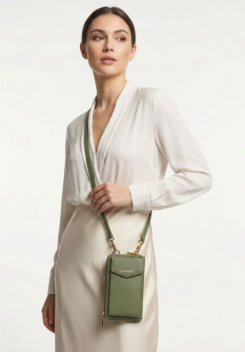 Mujer vestida con una blusa blanca y falda que lleva un bolso bandolera verde de cuero para teléfono con herrajes dorados y el logo "Lazarotti".