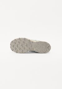 Mountain trail shoe sole in gray rubber, featuring prominent lug patterns for traction, with branding on the heel and sides.