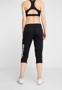 Svarta avkortade sweatpants med vit "SPP" text på vänster ben, tillverkade av ett mjukt material, med elastisk midja och åtsittande muddar.