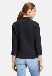 Zwarte, gestructureerde blazer met een kraag, driekwartmouwen en een getailleerde pasvorm, gecombineerd met lichtblauwe jeans.
