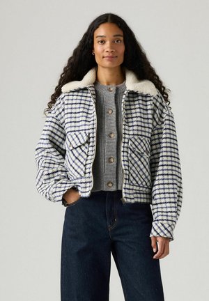 Vatteret hvid og blå ternet jakke med faux fur krave, lynlås lukning og to forlommer, båret over en grå striktrøje og mørke jeans.