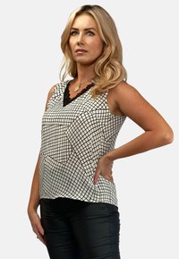 Czarny i biały bezrękawnik w kratę, z dekoltem w serek ozdobionym czarną koronką. Gładka tekstura materiału.