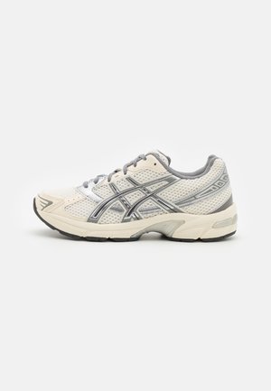 Chaussure de course en mesh blanc et gris avec fermeture à lacets et semelle noire, vue de côté sur un fond uni.