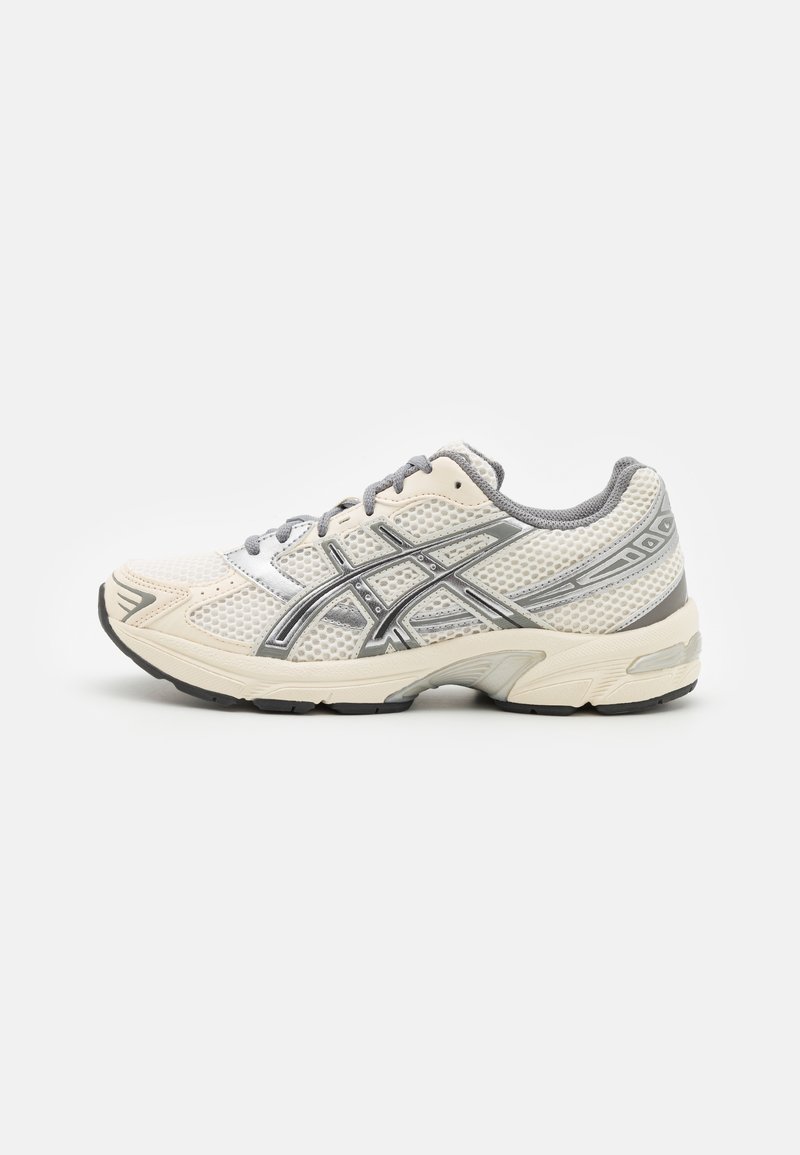 Chaussure de course en mesh blanc et gris avec fermeture à lacets et semelle noire, vue de côté sur un fond uni.