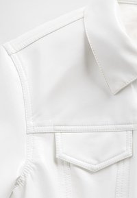 Balta dirbtinės odos striukė su smailia apykakle, išskirtiniu siuvimu ir priekyje esanti krūtinės kišenė su trikampe sklende.