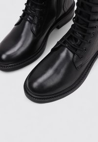 Black leather ankle boots with rounded toes, featuring lacing and stitched accents. Smooth surface with a durable rubber sole.