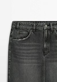 Jupe en jean noire avec poches avant, passants pour ceinture et fermeture par bouton sur fond blanc.