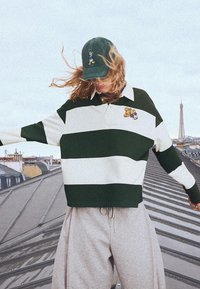 Grön och vit randig tröja med krage, med en tecknad karaktär på bröstet. Matchas med grå, löst sittande mjukisbyxor.