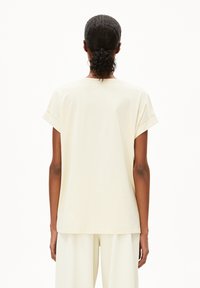 Helles beige T-Shirt mit kurzen, umgeschlagenen Ärmeln und lockerer Passform. Weicher, glatter Stoff mit einem schlichten Design und einem unauffälligen Rücken.